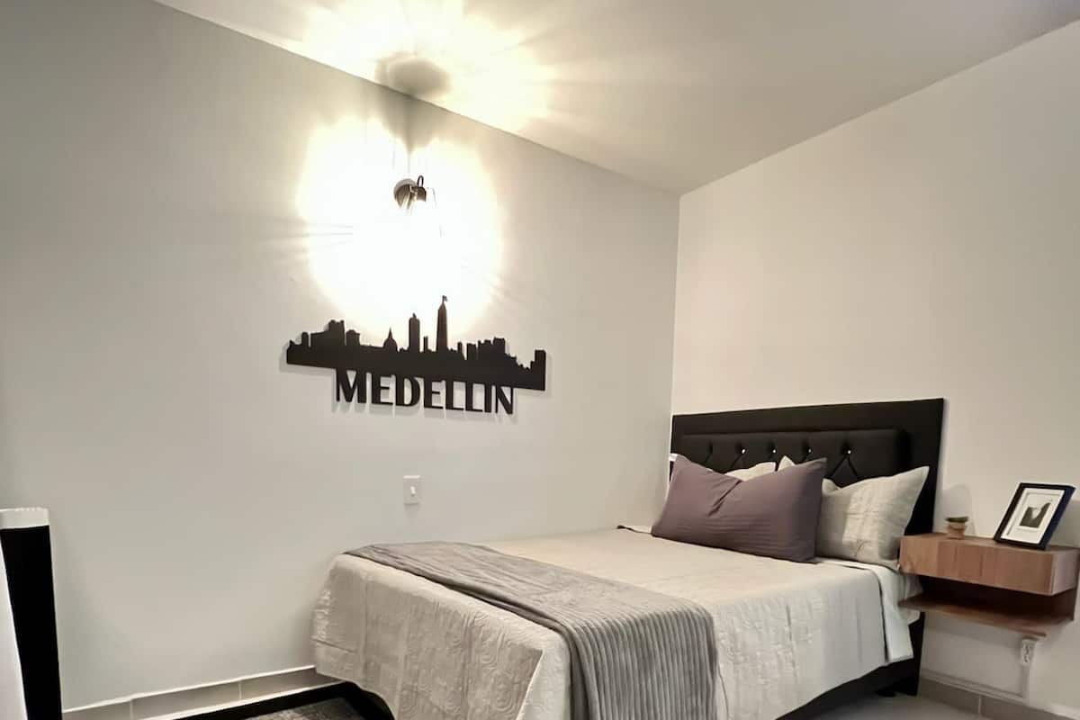 Ein Schlafzimmer mit Bett, Nachttisch, Wandleuchte und einer Skyline-Motivierung.