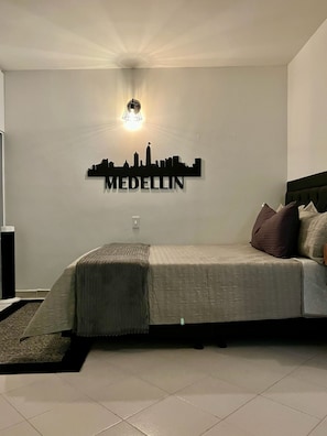 Une chambre à coucher avec un lit, des oreillers, une lampe fixée au mur et un autocollant représentant une vue panoramique de la ville.
