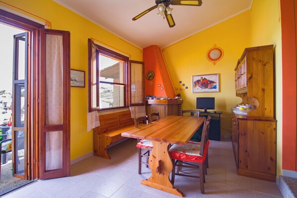 Un coin repas avec une table et des chaises en bois, un banc, un ventilateur de plafond et une fenêtre avec des rideaux.