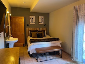 Un dormitorio con cama, puerta de madera, lavamanos y un banco.