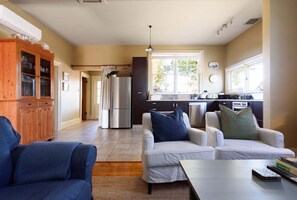A modern kitchen with a refrigerator, stove, and sink. There are two white sofas with blue cushions and a blue armchair.