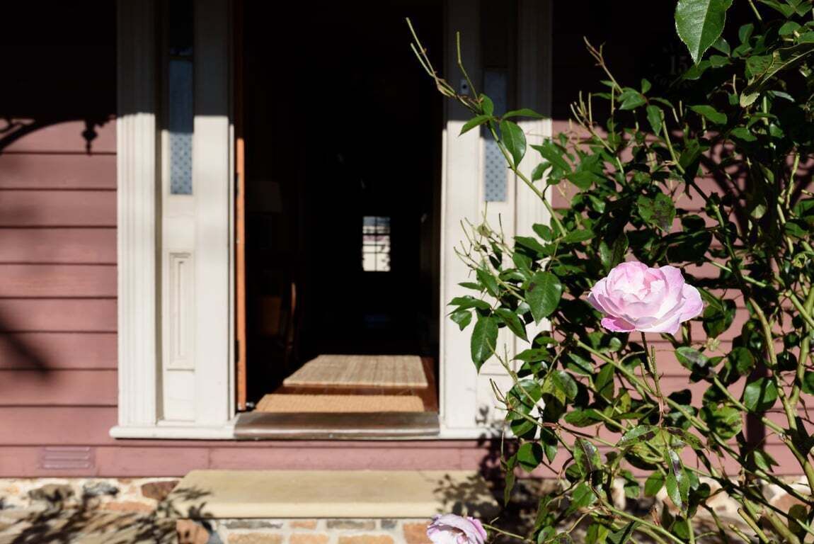 Una entrada de casa con un porche de madera, una rosa rosa y una ventana que da al interior.