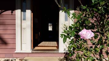 Una entrada de casa con un porche de madera, una rosa rosa y una ventana que da al interior.