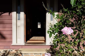 A house entrance with a wooden porch, a pink rose, and a window with a view into the house.