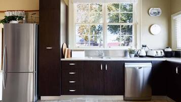 Una cocina moderna con un refrigerador de acero inoxidable, armarios oscuros, lavavajillas y una ventana con vistas a árboles.