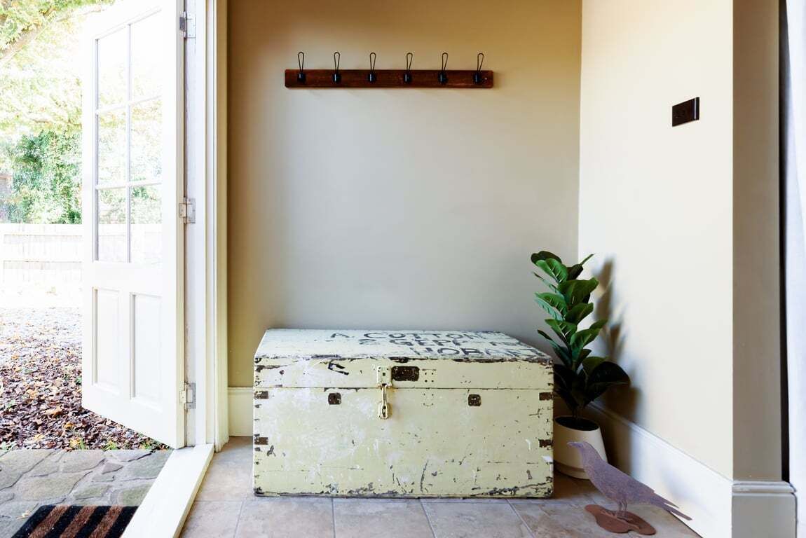 A room with a white door, a coat rack, a green plant, and a vintage suitcase.