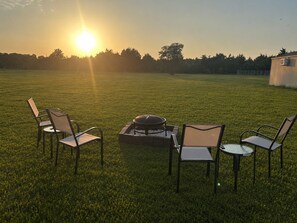 A grassy outdoor area with a fire pit and four chairs arranged around it.