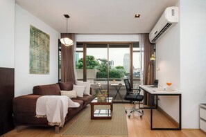 Eine moderne Wohnung mit Sofa, Schreibtisch, Stuhl und Blick auf die Stadt durch große Fenster.