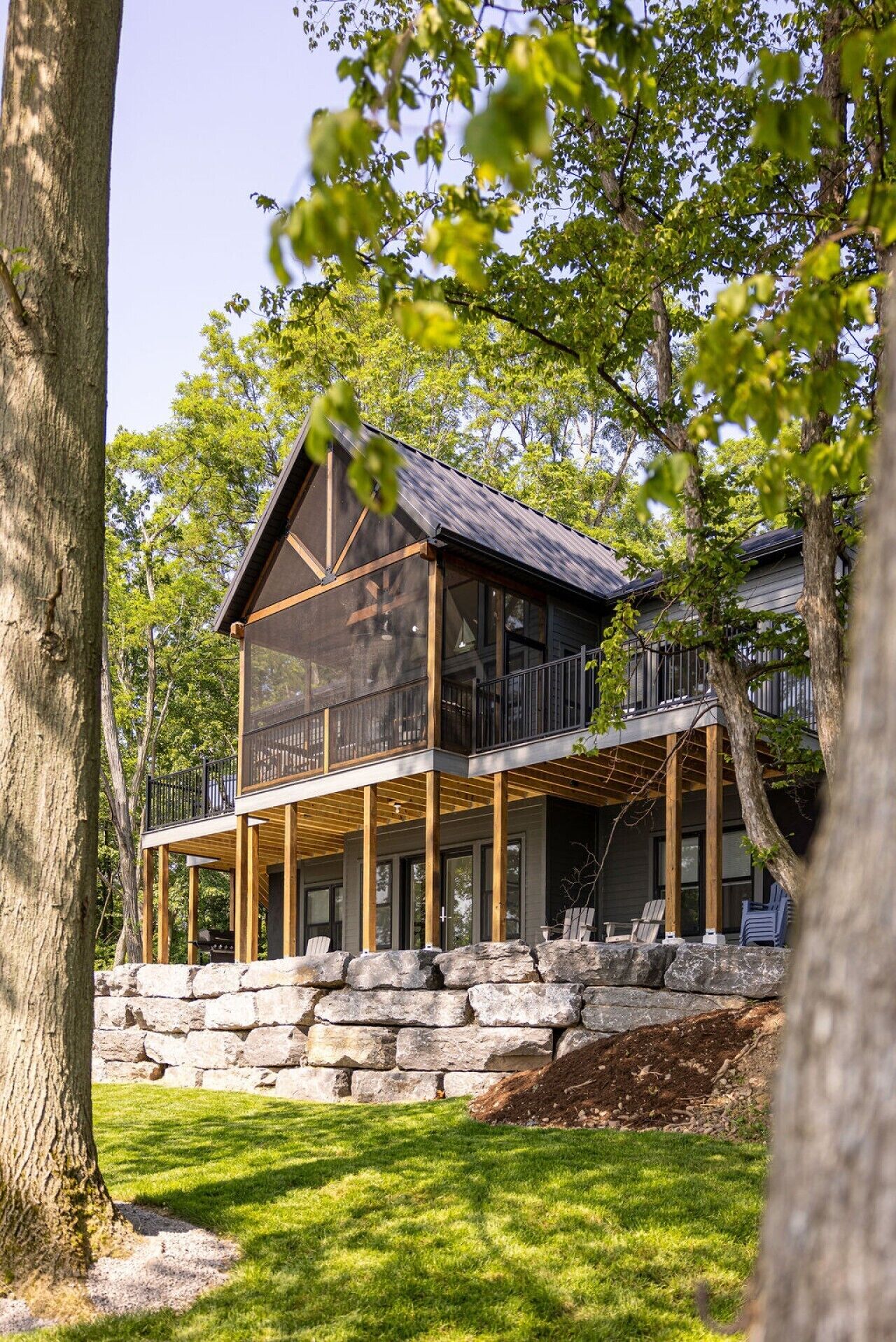 Una casa moderna de dos pisos con base de piedra, terraza de madera y un balcón grande.