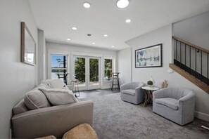 Un salón amplio con un sofá gris, dos sillones, una mesita y una escalera.