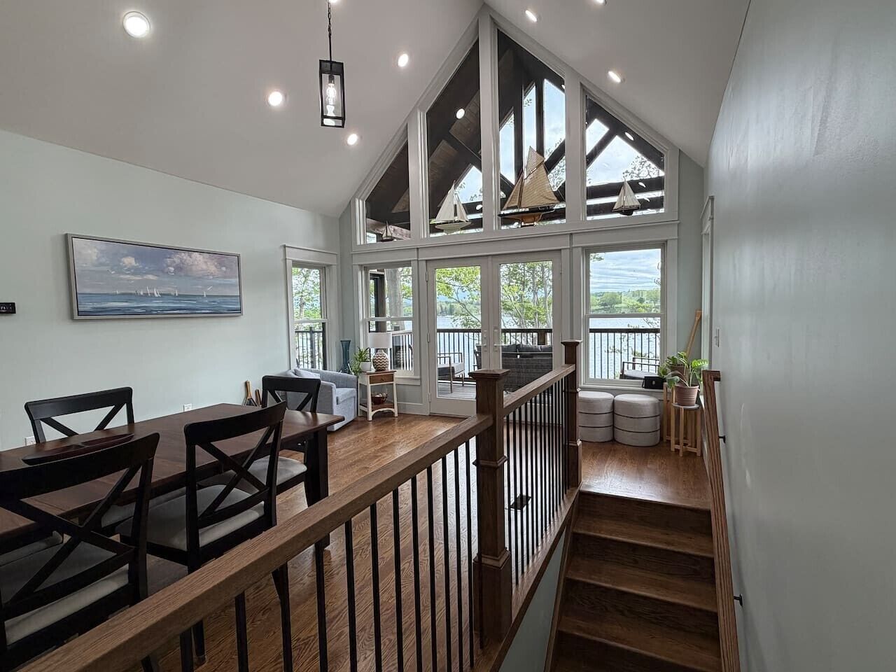 Un comedor espacioso con techo alto y ventanas grandes, una escalera que lleva a una cubierta superior y vistas al exterior.