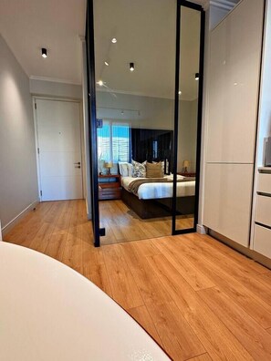 A bedroom with a bed, bedside tables, a wardrobe, and a mirror. - Elite Executive Suite | Ellipse | Waterfall City (Midrand)