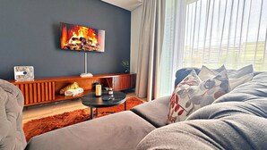 Una sala de estar moderna con un televisor grande montado en la pared, un sofá, una mesita de centro y una chimenea.
