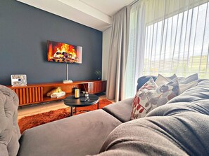 A modern living room with a large TV mounted on the wall, a sofa, a small coffee table, and a fireplace. - Elite Executive Suite | Ellipse | Waterfall City (Midrand)