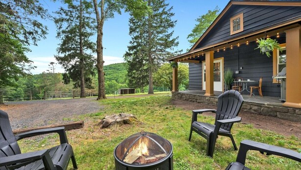 Une cabane en bois avec un foyer extérieur, des sièges de jardin et une véranda couverte.
