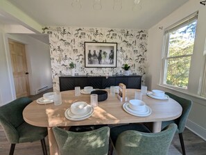 Un comedor con una mesa redonda dispuesta para cuatro personas, sillas tapizadas en verde, un sofá negro y una pared con papel tapiz de caballos.