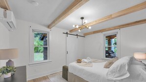 Une chambre à coucher comprenant un lit, des tables de chevet, un ventilateur de plafond et une fenêtre donnant sur un paysage verdoyant.