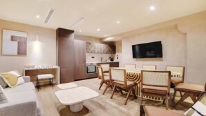 Uma sala de estar moderna com área de jantar, cozinha ao fundo e televisão de tela plana na parede.