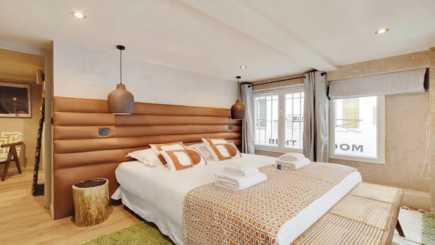 Quarto de hotel moderno com uma cama grande, cabeceira de madeira, mesa de cabeceira pequena e uma janela com cortinas.