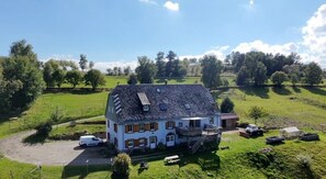 Et stort hus med et stejlt tag, en veranda og et mindre tilbygning.
