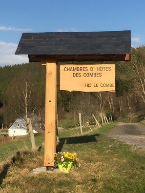 A wooden signpost with a yellow sign indicating 'CHAMBRES D'HOTES DES COMBES 185 LE COMBE' in a rural setting with a house in the background. - Guest House 'Chambre Familiale - Kalie-Simba' with Mountain View and Shared Garden (Orbey)