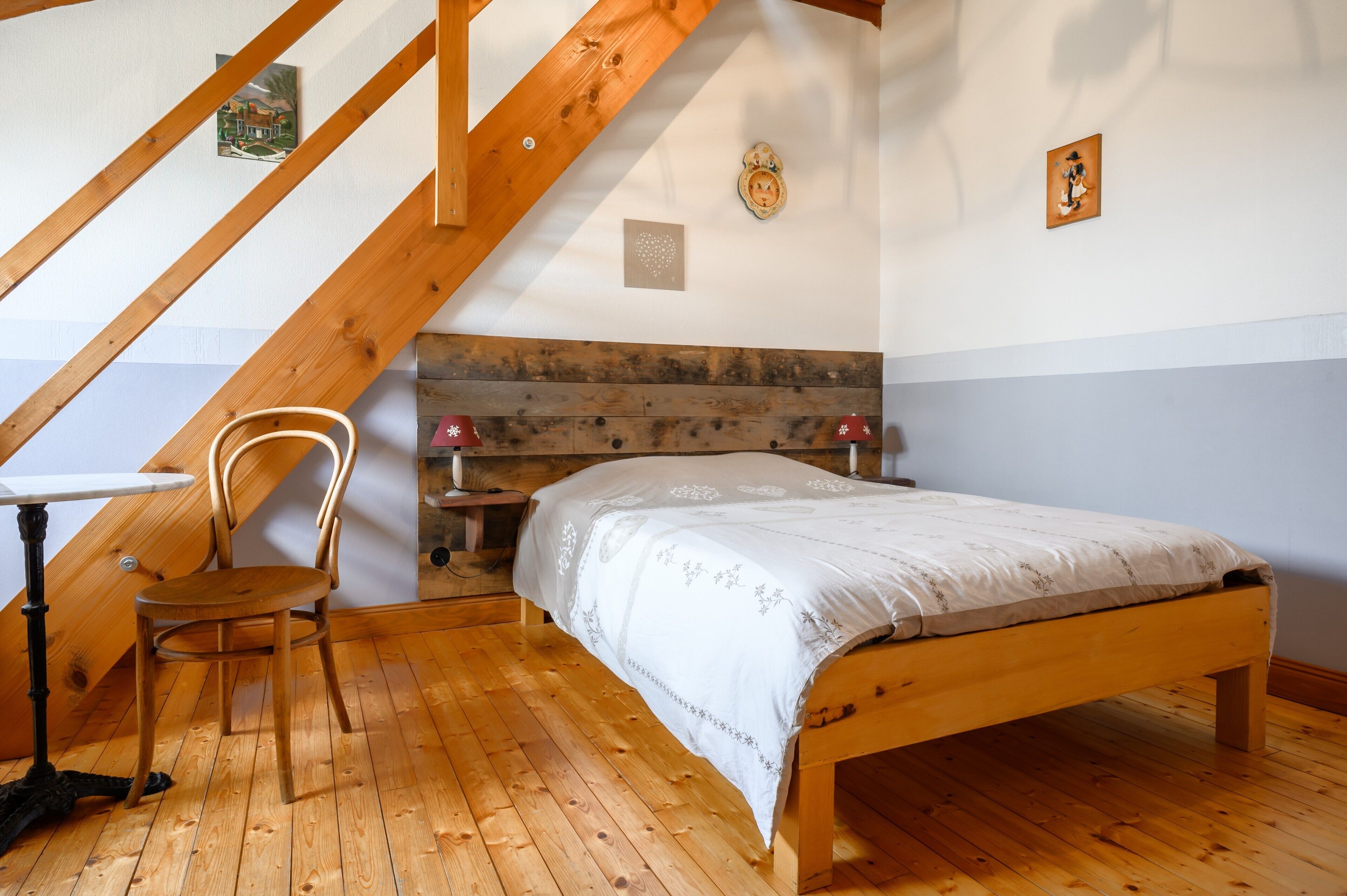 Une chambre à coucher avec un lit en bois, une chaise, une petite table et un escalier en bois.