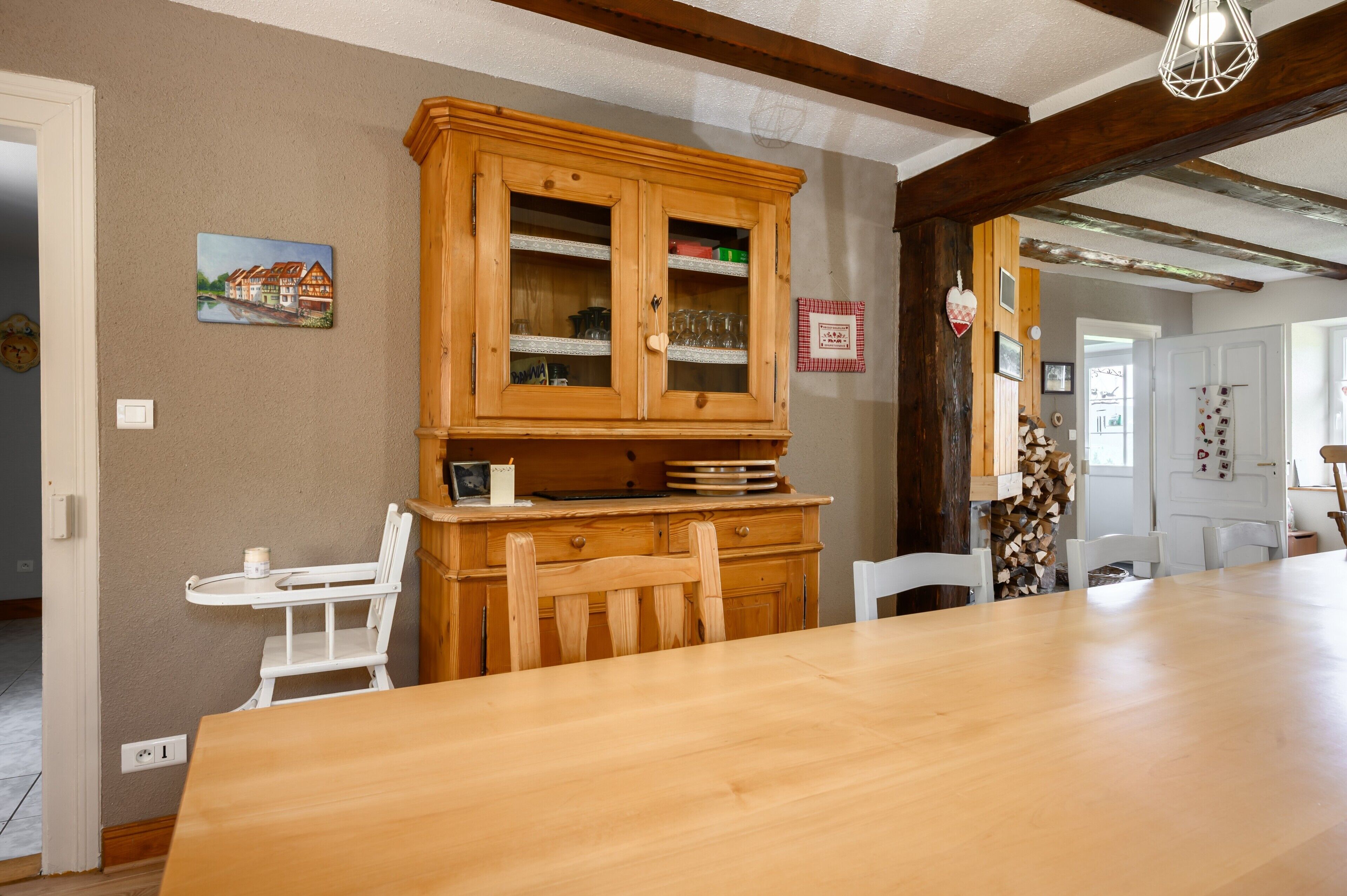 A dining area with a wooden table, chairs, a cabinet with glass doors, and a painting on the wall.