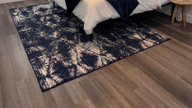 Een slaapkamer met een bed, een plafondventilator, een raam met zonwering, een aan de muur hangend abstract schilderij en een klein nachtkastje met een plant.