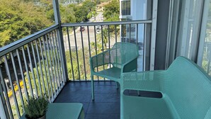 Een balkon met twee groene stoelen en een tafel, een potplant en uitzicht op een woongebied.