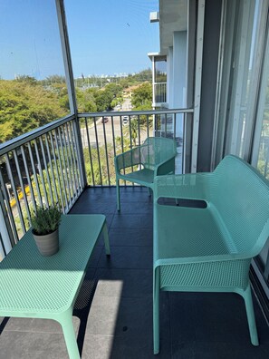 Ein Balkon mit zwei grünen Stühlen und einem Tisch, einem Blumentopf und Blick auf eine Wohngegend.