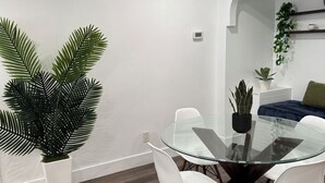 Een moderne eethoek met een glazen tafel, witte stoelen, een potplant en een trap.
