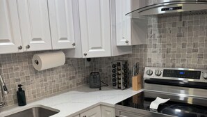 Een moderne keuken met witte kasten, een roestvrijstalen afzuigkap, een inbouwoven en een betegelde spatwand.