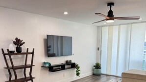 Een moderne woonkamer met een flatscreen televisie, houten vloer, een plafondventilator en een groene fauteuil.