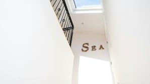 Eine Treppe führt zu einem Raum, der mit einem 'SEA'-Schild, einem Oberlicht und einer weißen Wand gekennzeichnet ist.