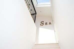 Eine Treppe führt zu einem Raum, der mit einem 'SEA'-Schild, einem Oberlicht und einer weißen Wand gekennzeichnet ist.
