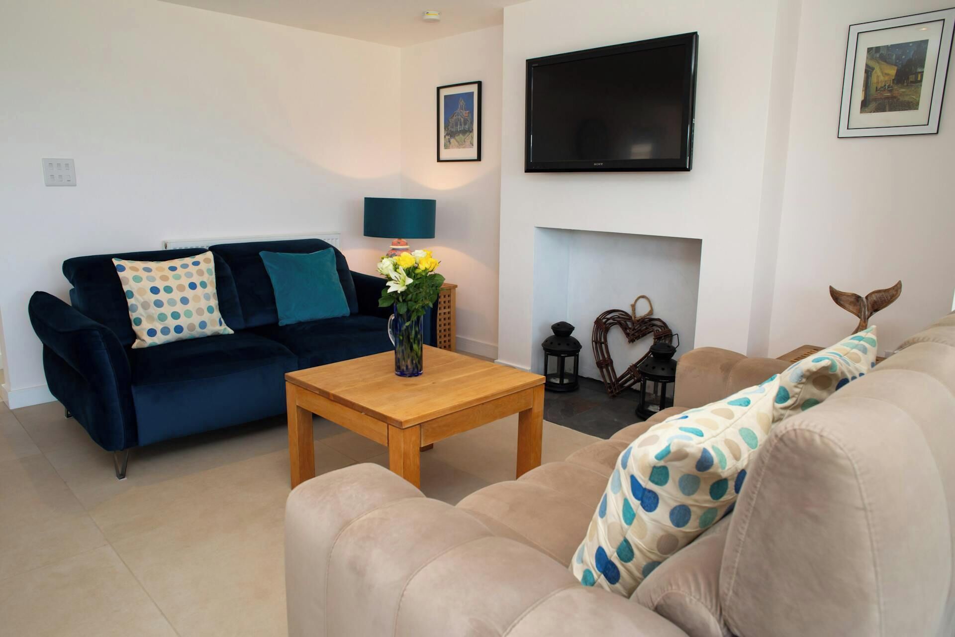 A living room with a dark blue sofa, a beige sofa, a wooden coffee table, a flat-screen TV mounted on the wall, and a fireplace.