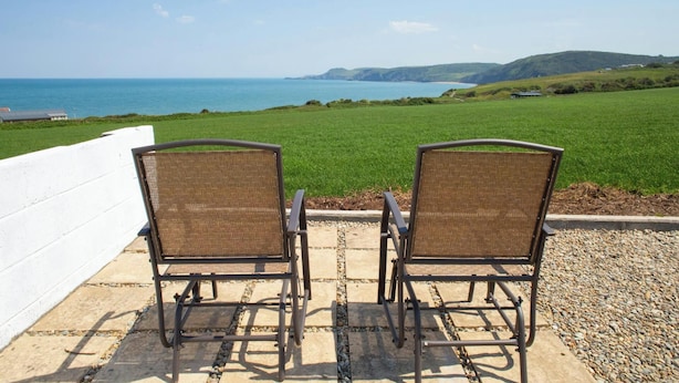 Zwei Korbstühle mit Blick auf das Meer und grüne Felder.