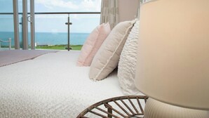 Ein Schlafzimmer mit großem Fenster, einem Bett mit weißer Bettwäsche und Meerblick.