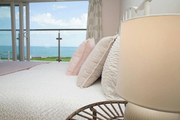 Ein Schlafzimmer mit großem Fenster, einem Bett mit weißer Bettwäsche und Meerblick.