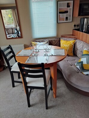 A dining area with a round table, chairs, and a sofa with cushions. - Stay 6 - Pool - Parking - Beachside - Pet Friendly (Norwich)