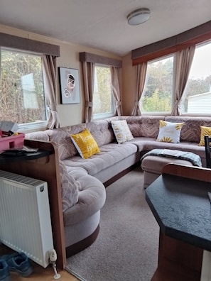 A cozy living area with a sofa, cushions, a radiator, and a window with curtains. - Stay 6 - Pool - Parking - Beachside - Pet Friendly (Norwich)
