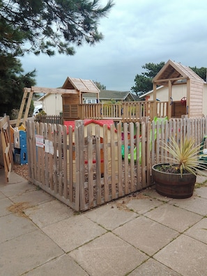 A fenced outdoor play area with wooden playhouses and a climbing structure. - Stay 6 - Pool - Parking - Beachside - Pet Friendly (Norwich)