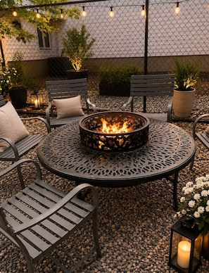 A round metal table with a fire pit in the center, surrounded by metal chairs with cushions.