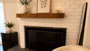 Un salon avec une cheminée en briques blanches, un téléviseur à écran plat, un fauteuil en cuir et un tapis en peau de vache.