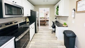 A kitchen with white cabinets, a microwave, stove, refrigerator, and a trash can. - Beautiful Eastgate 12B (Hammond)