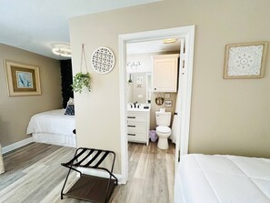 Un dormitorio con cama, una silla, un baño con inodoro y lavamanos, y un pasillo.