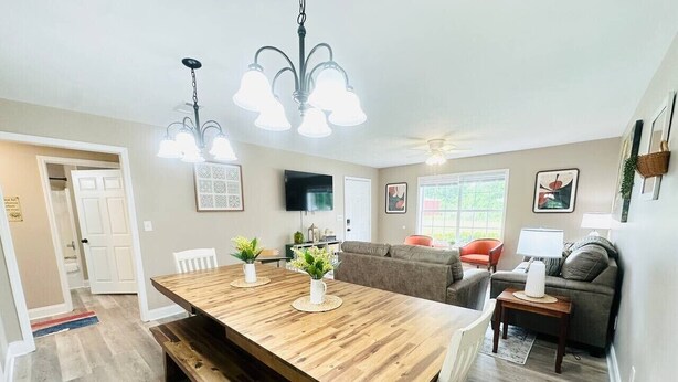 A dining area with a wooden table, benches, and a chandelier. There is a sofa and a television in the background. - Beautiful Eastgate 12B (Hammond)