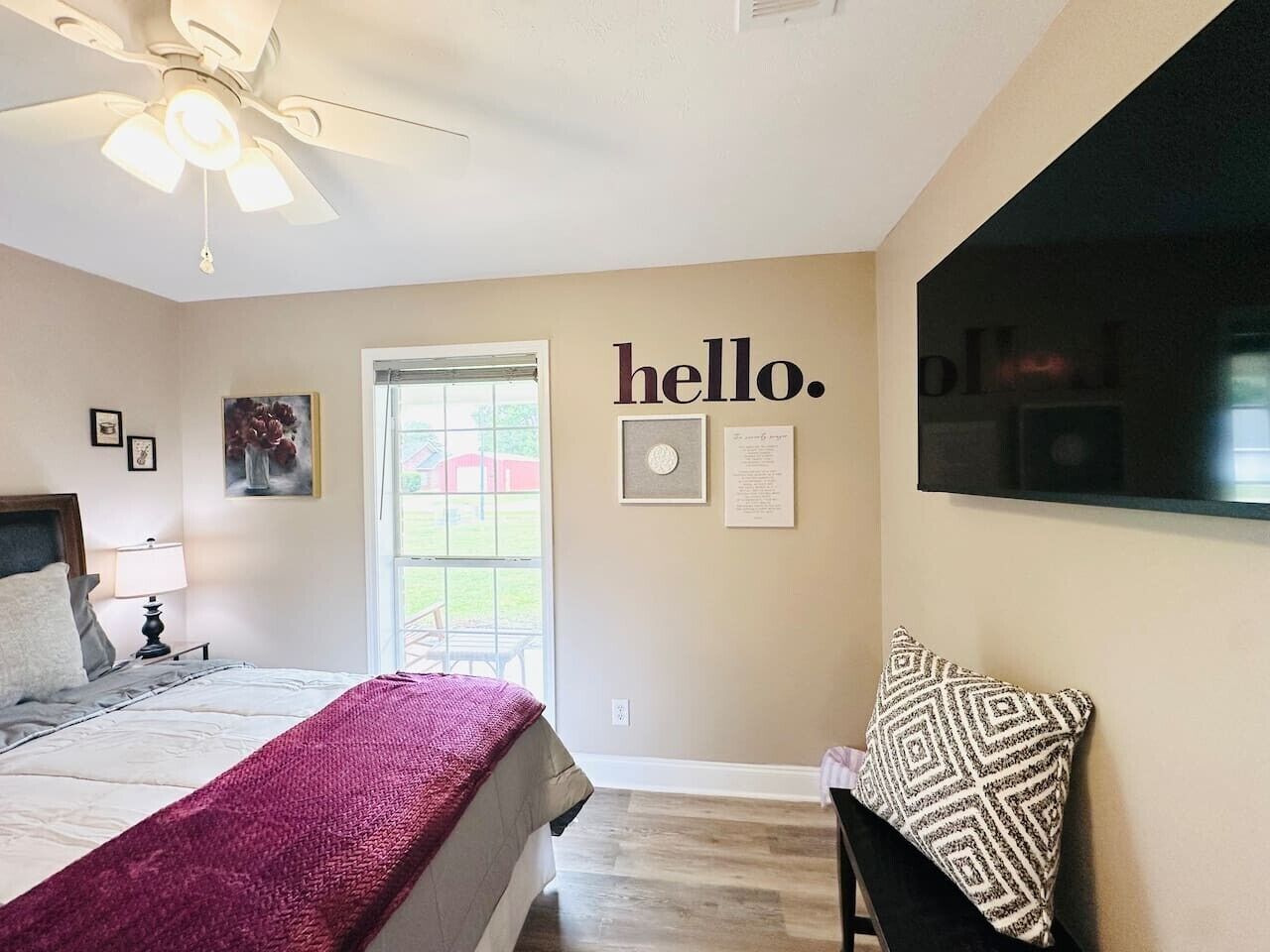 Un dormitorio con cama, una silla, un ventilador de techo, una ventana y una pared con un cartel que dice 'hello'.