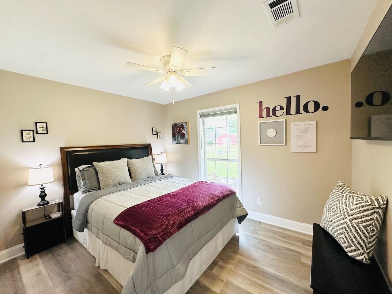 A bedroom with a bed, nightstands, a ceiling fan, a window, and a wall with a 'hello.' sign.
