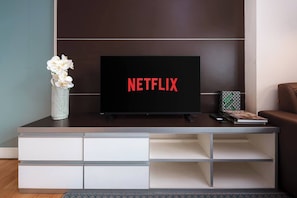 Ein modernes Wohnzimmer mit einem Flachbildfernseher, der das Netflix-Logo zeigt, einer dekorativen Vase mit Blumen und einem Buch auf einem Beistelltisch.